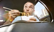 Man eating noodles from box sitting in car