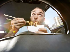 Man eating noodles from box sitting in car