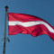 The Flag of Latvia waving in the wind with a clear blue sky.